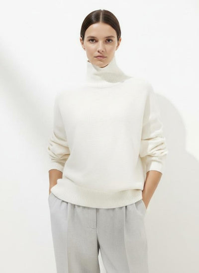 Person wearing a white turtleneck sweater and light gray pants on a white background