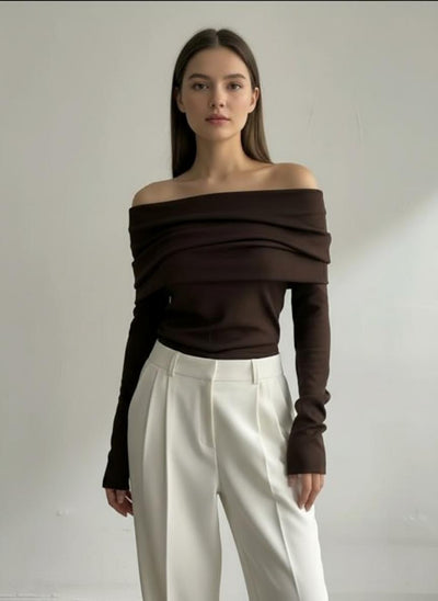 Woman wearing a brown off-shoulder top and white pants against a plain background