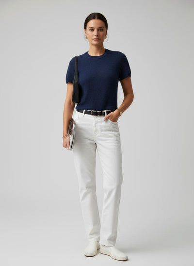 Woman wearing a navy blue t-shirt, white pants, and white shoes on a plain background