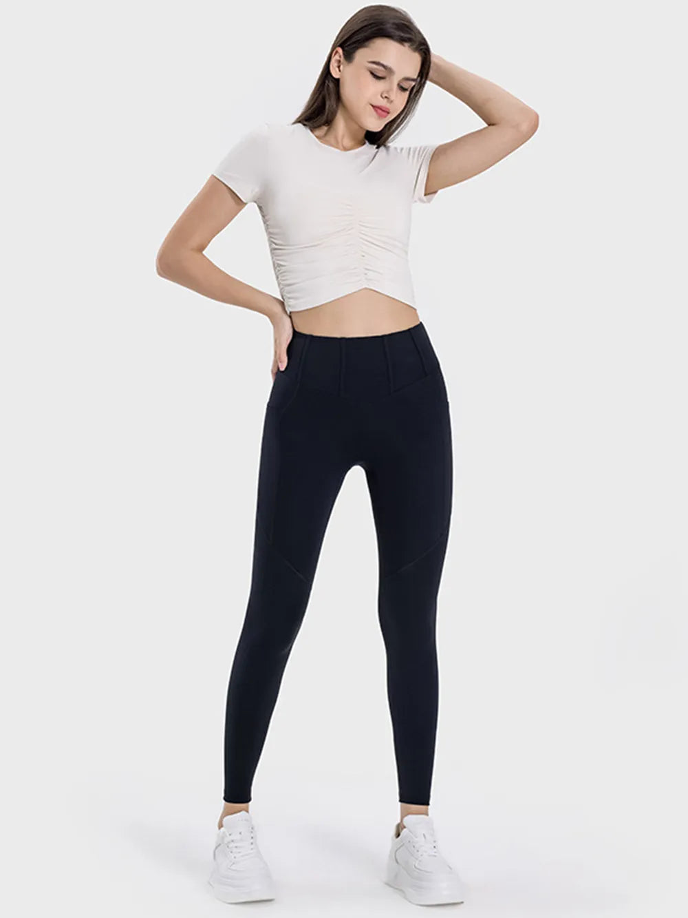 Woman wearing a white crop top and black leggings on a white background