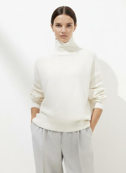Person wearing a white turtleneck sweater and light gray pants on a white background