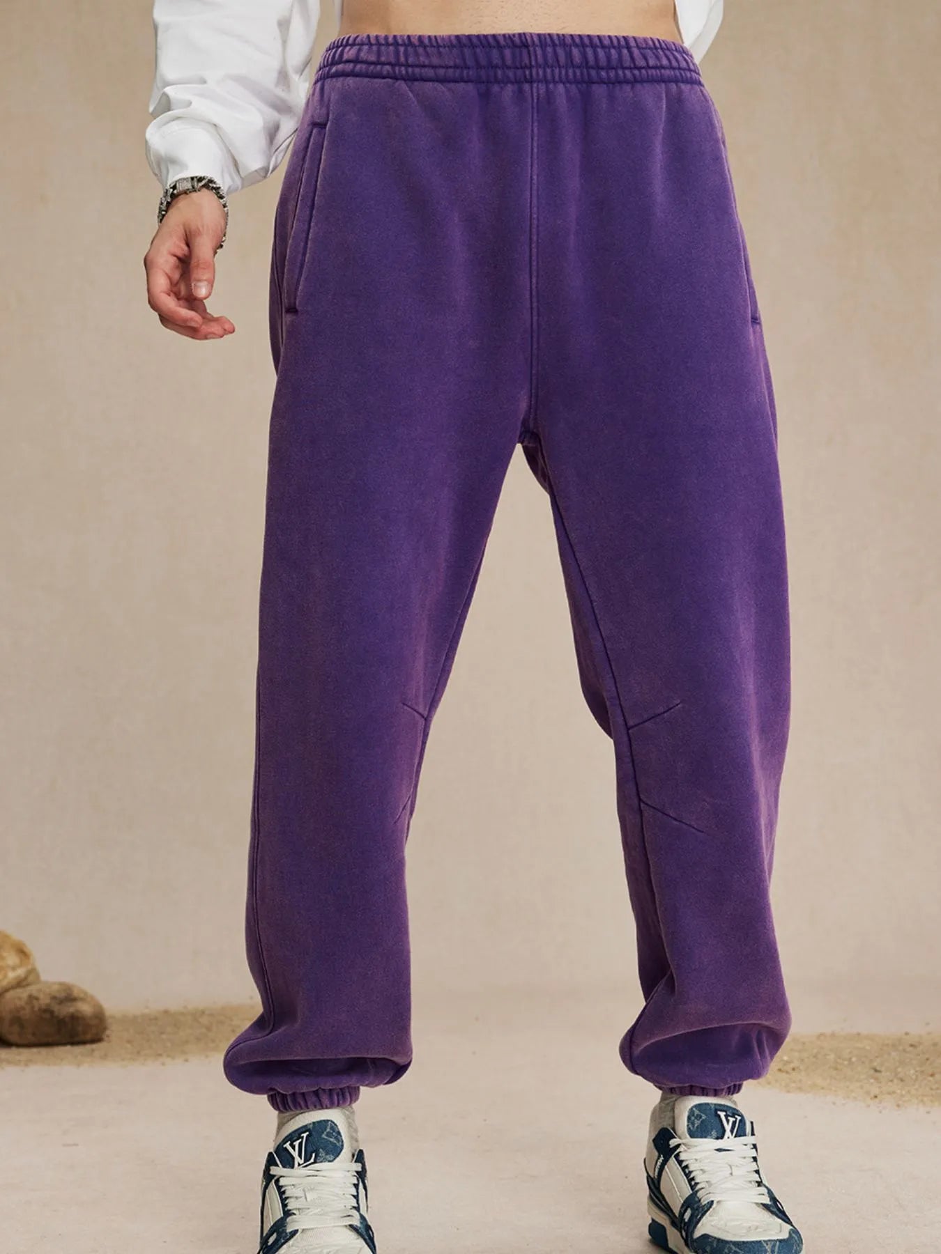 Purple sweatpants worn by a person on a beige background
