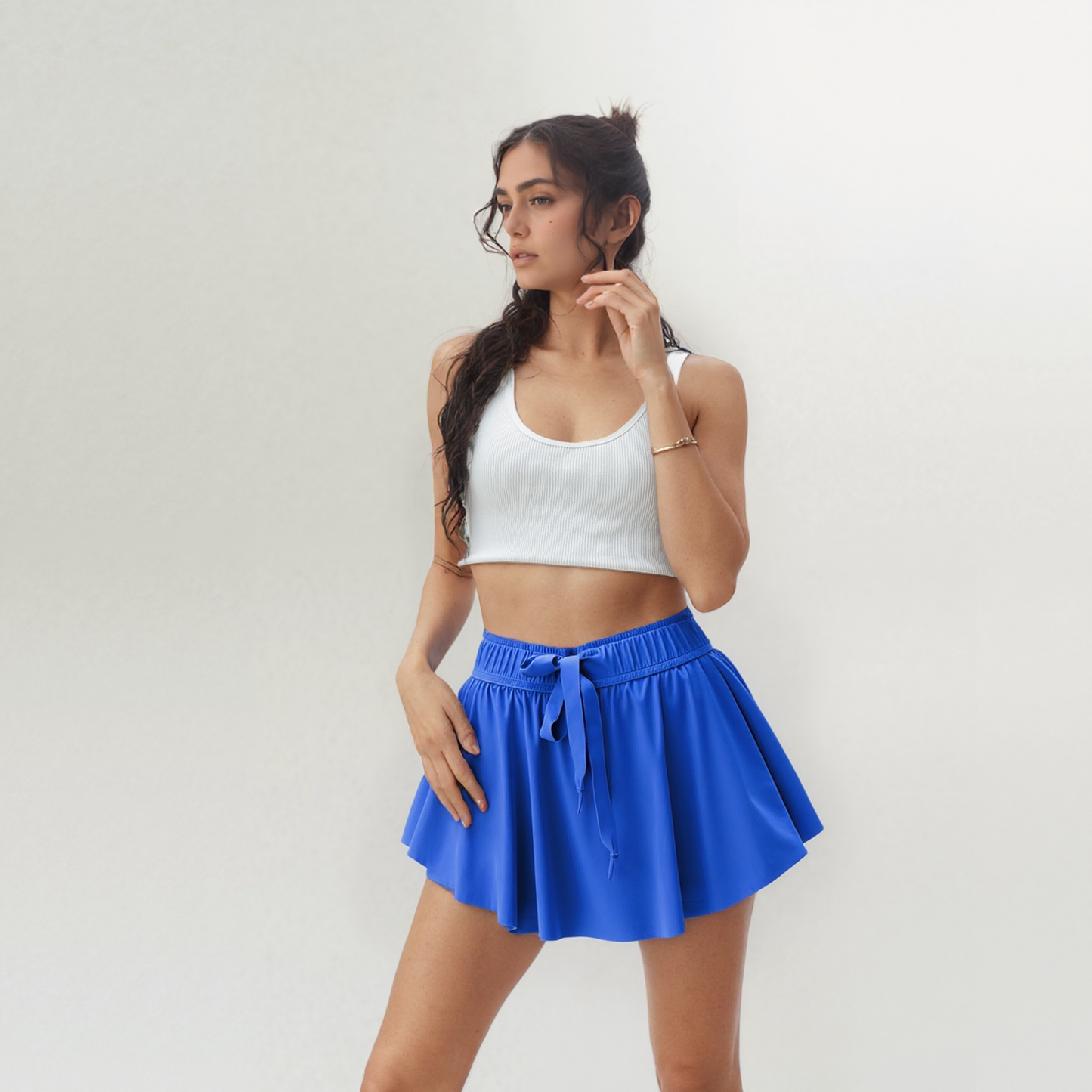 Woman wearing a white crop top and blue skirt against a plain background