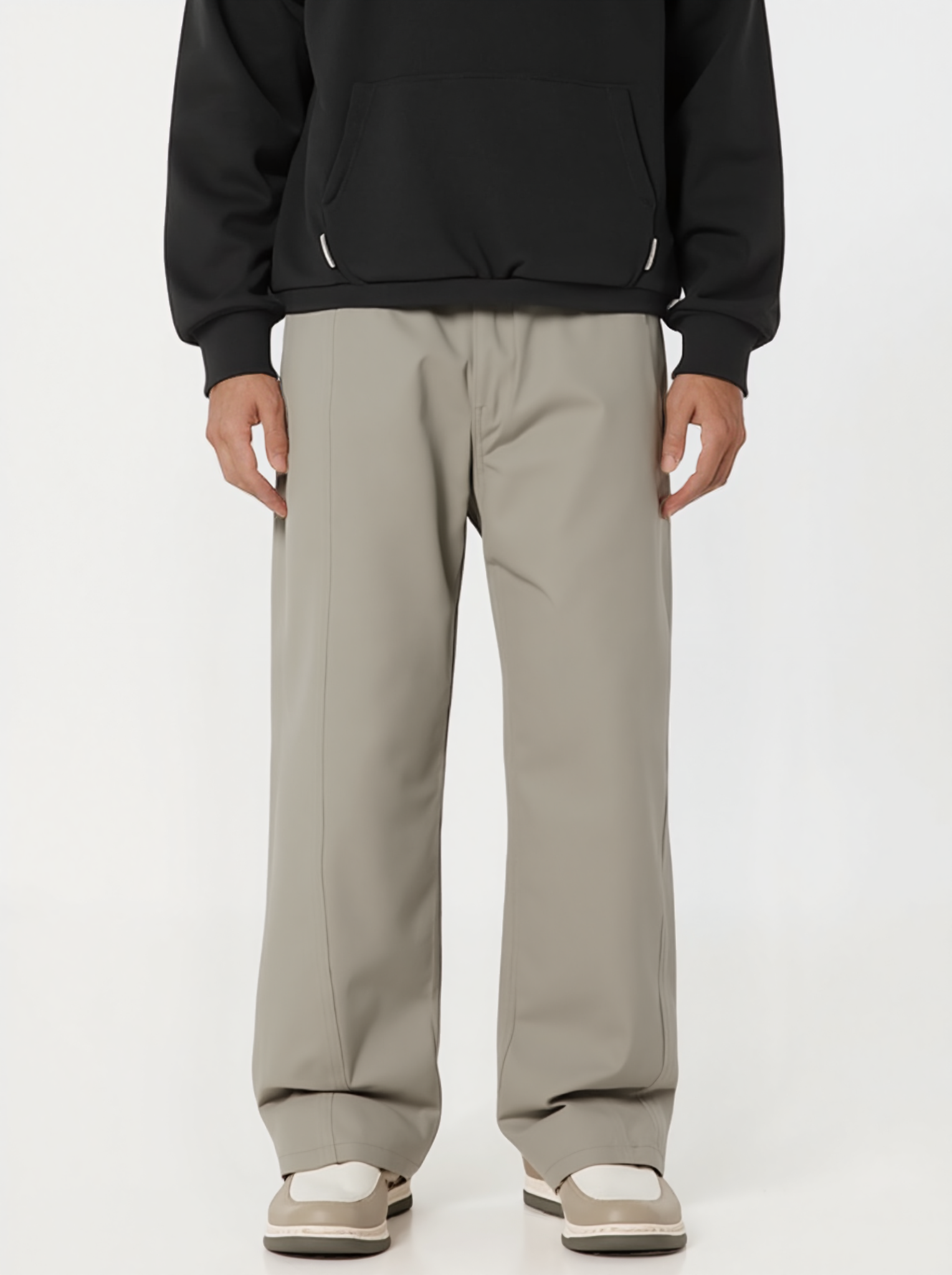 Person wearing a black hoodie and beige pants on a white background