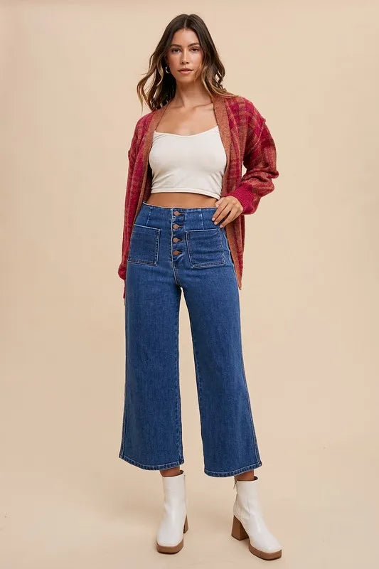 Woman wearing a red plaid shirt, white top, blue jeans, and white boots on a beige background