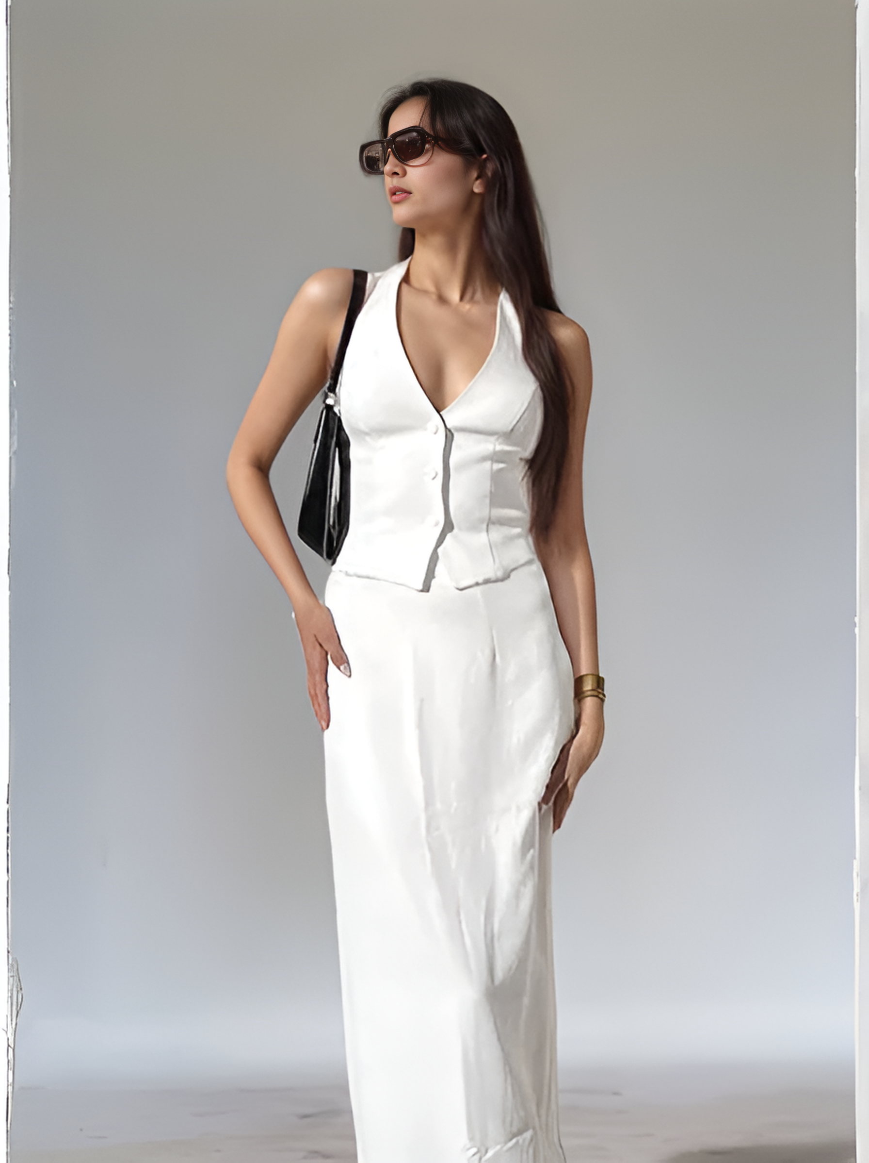 Woman in a white outfit with sunglasses and a black handbag against a plain background