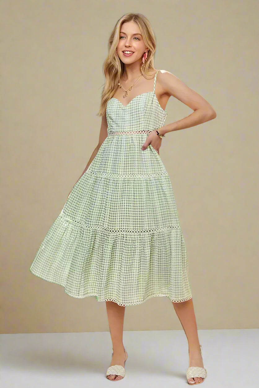 Woman wearing a green checkered dress in a bright room with a plant and chair.