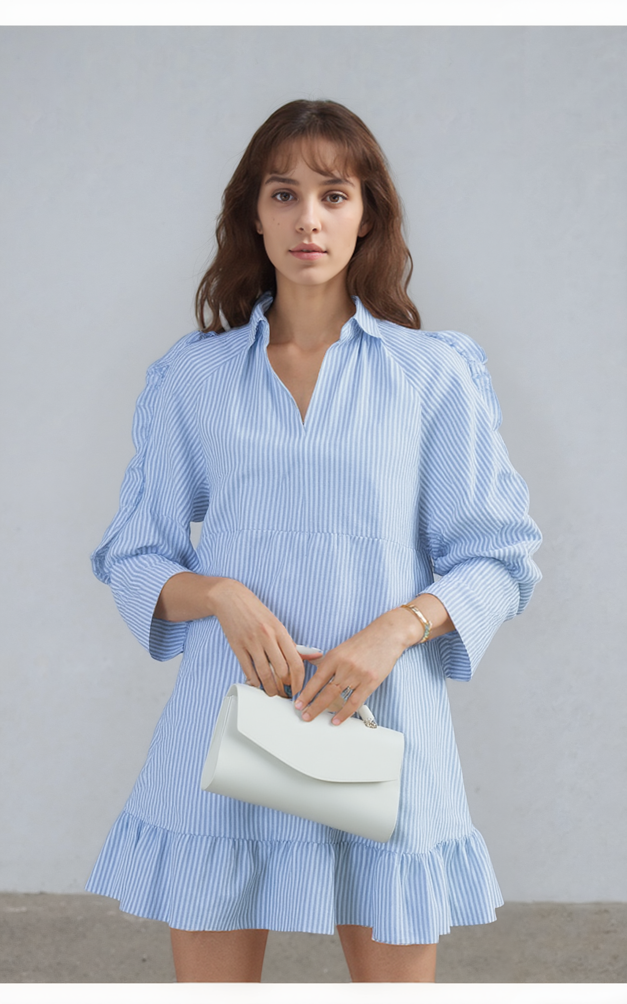 Woman wearing a light blue and white striped dress holding a white clutch against a plain background