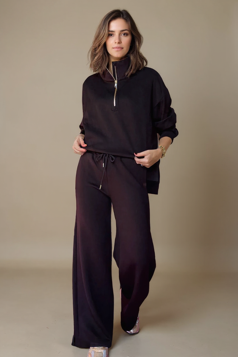 Woman wearing a black outfit with a high collar and wide-leg pants on a beige background
