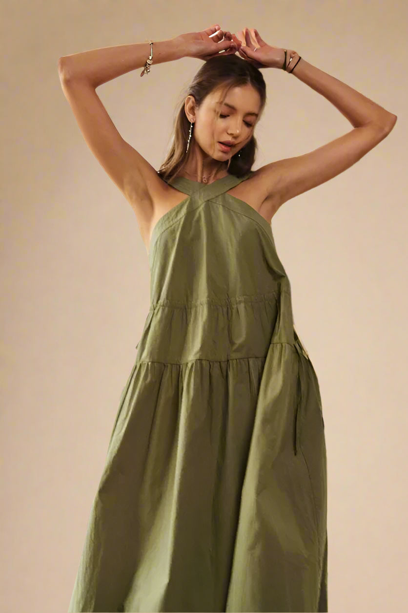 Woman wearing a green dress standing indoors with a window and plant in the background