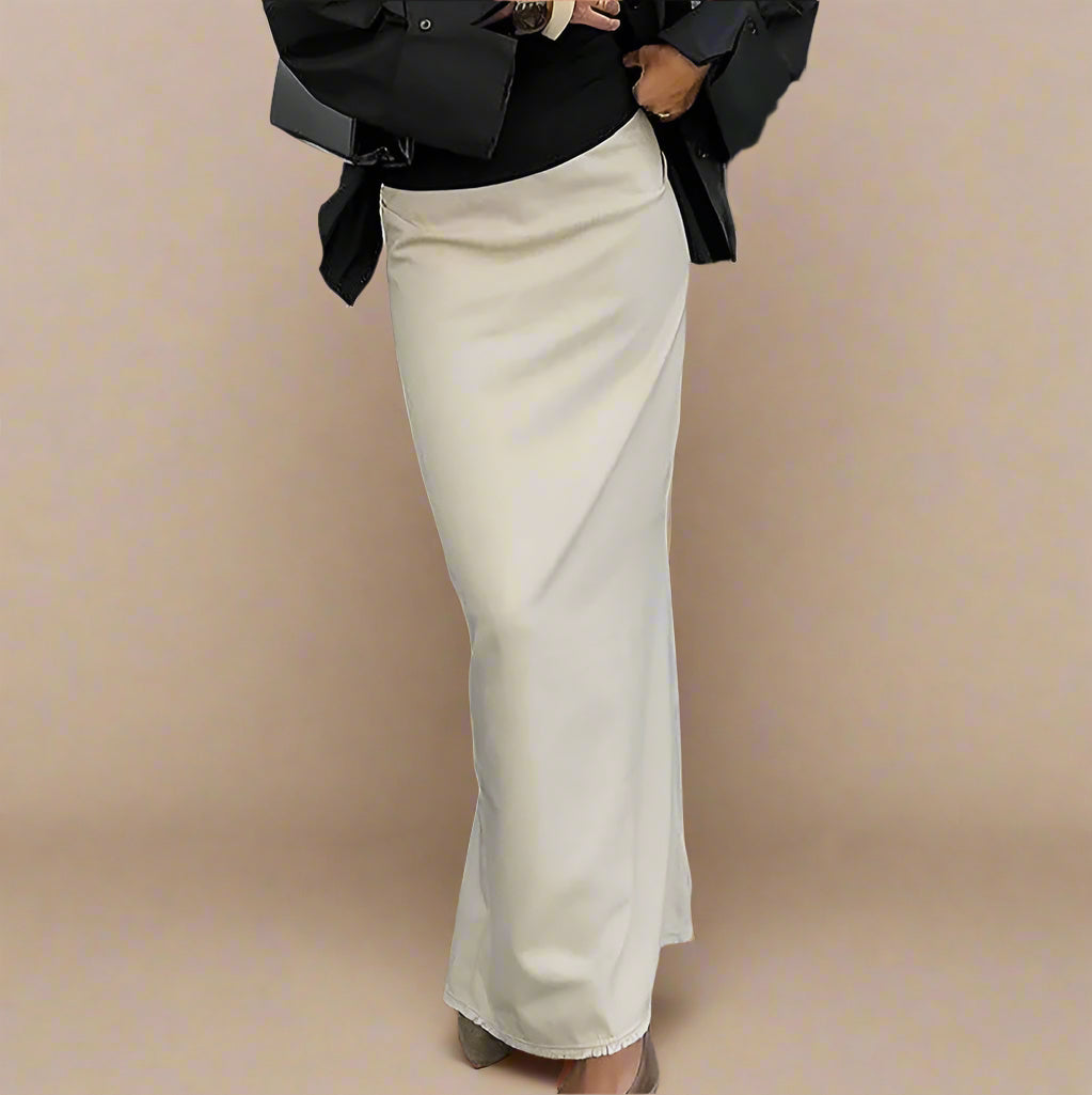 Person wearing a black top and beige skirt standing on a sidewalk.