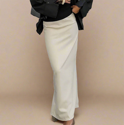 Person wearing a black top and beige skirt standing on a sidewalk.