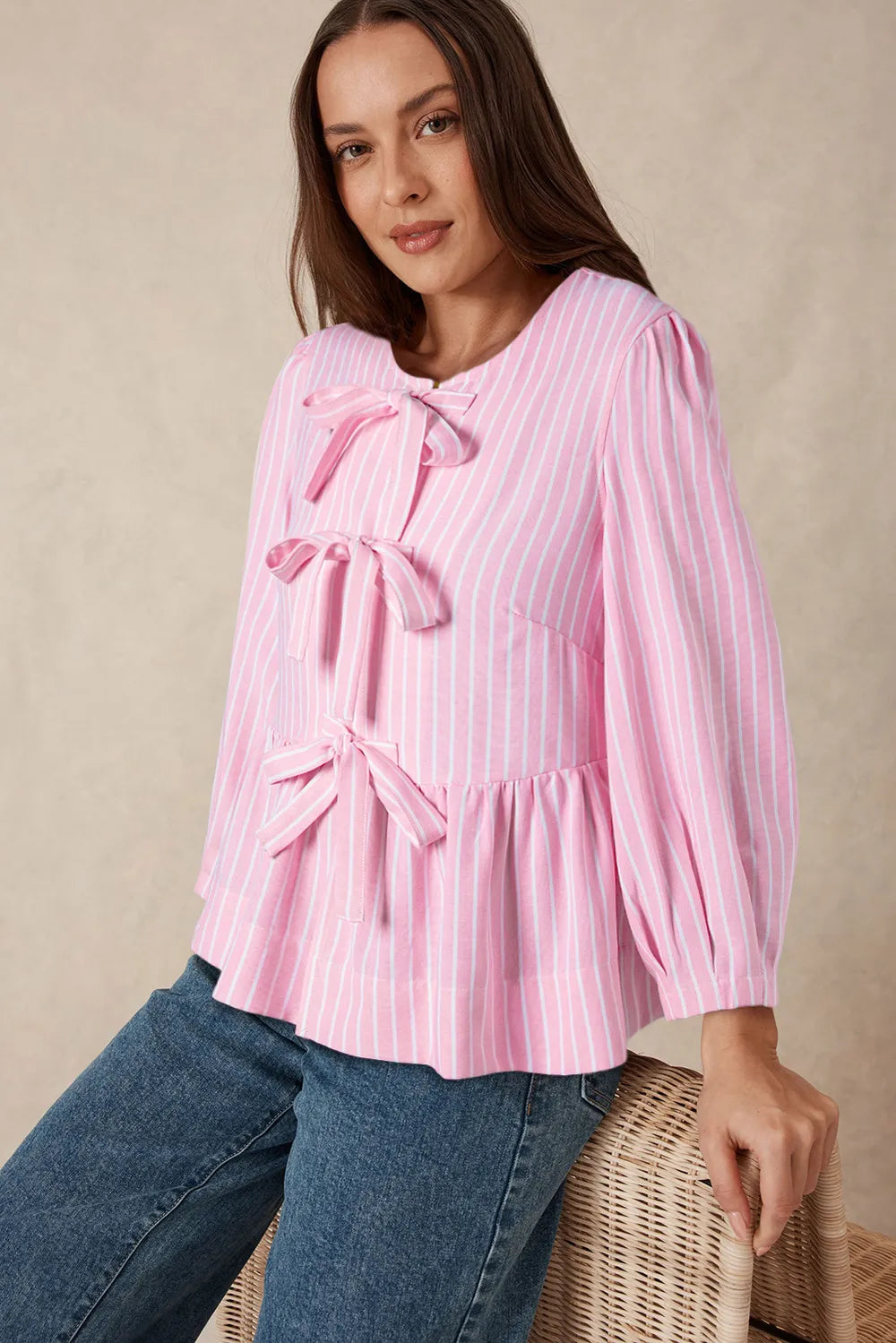 Woman wearing a pink striped blouse with bow details against a beige background